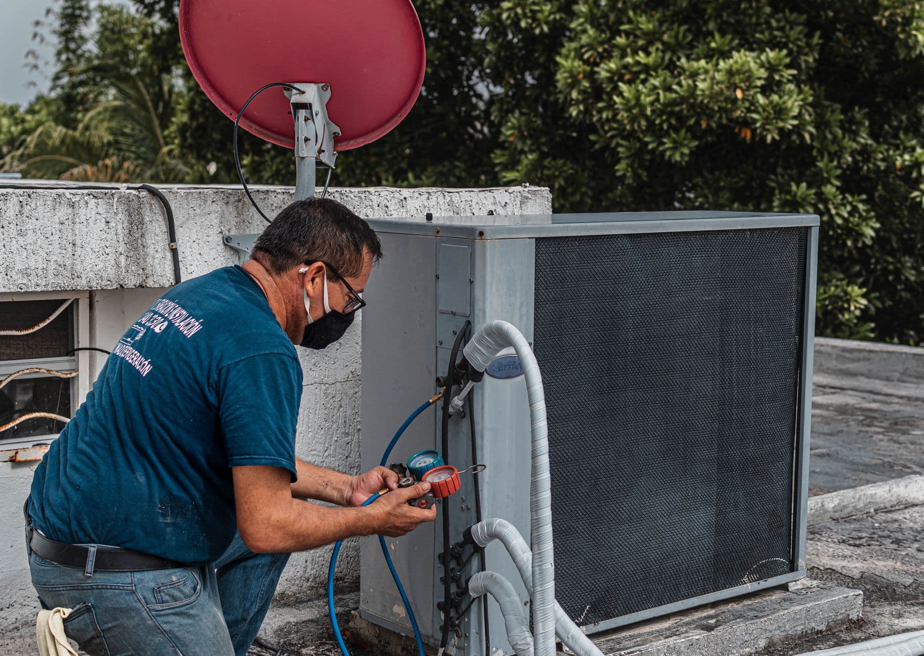 An HVAC technician using a manifold gauge to service a rooftop air conditioning unit