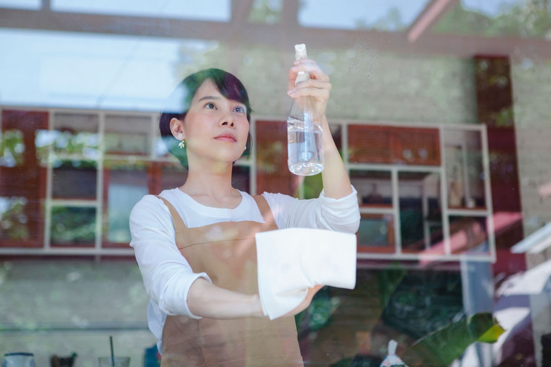 A cleaner wiping down a glass surface with a spray bottle and cloth